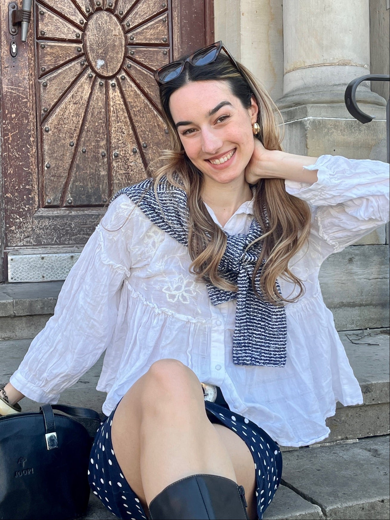 Mädchen in weißer Bluse sitzt auf einer Treppe vor einer Holztür und lacht 